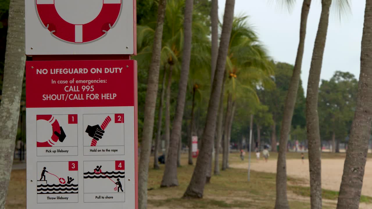 Plano médio estático de uma placa vermelha de segurança de praia entre palmeiras em Singapura