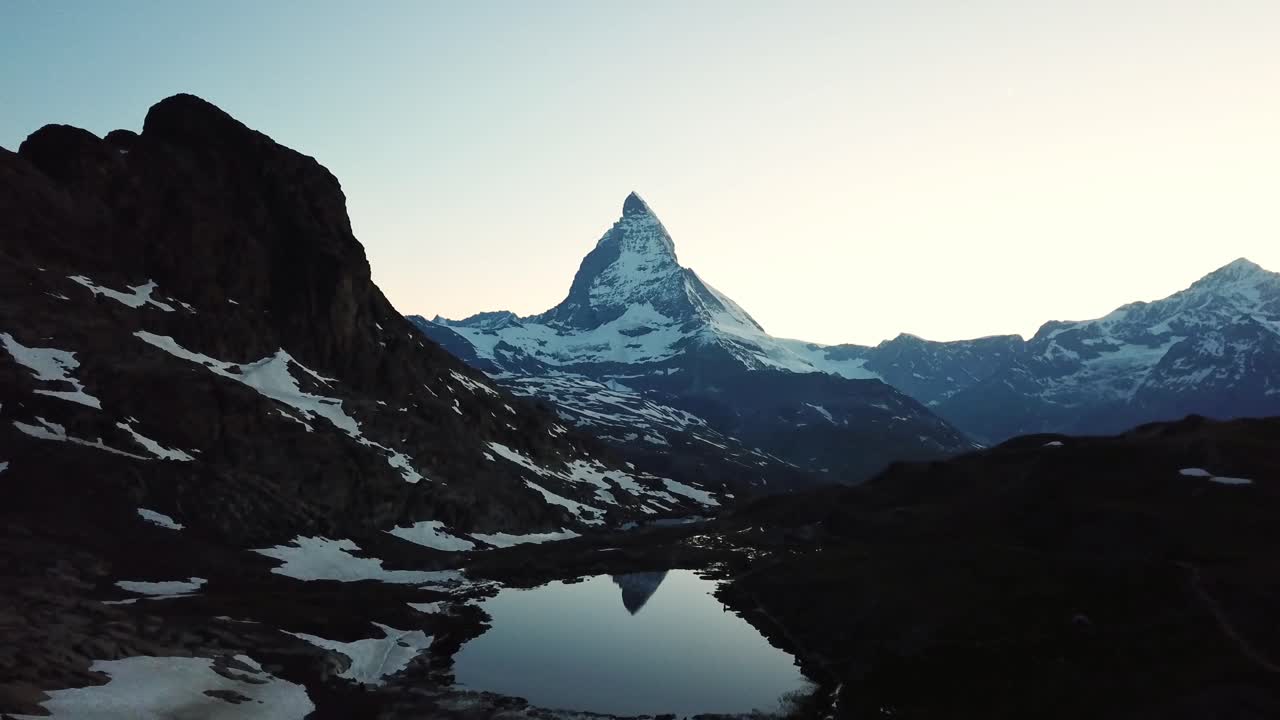 Drone pull out shot capturing majestic Matterhorn peak at dawn, reflecting in Riffelsee serene lake amid alpine landscape, Wallis, Switzerland