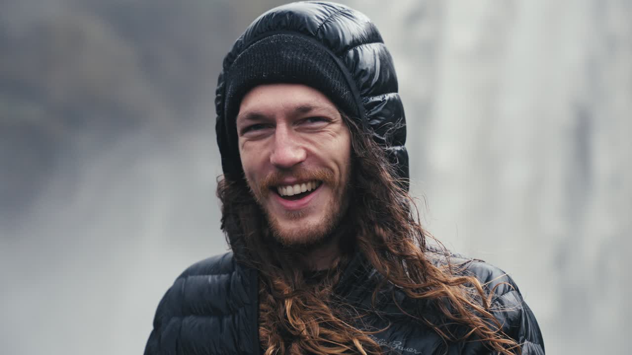 un excursionista masculino frente a una cascada sonríe al aire libre