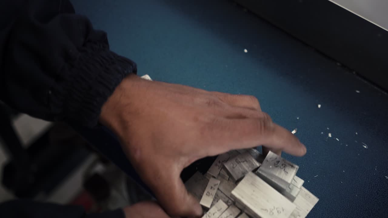 Close-up of a Person's Hands Handling Small Metal Blocks in a Workshop