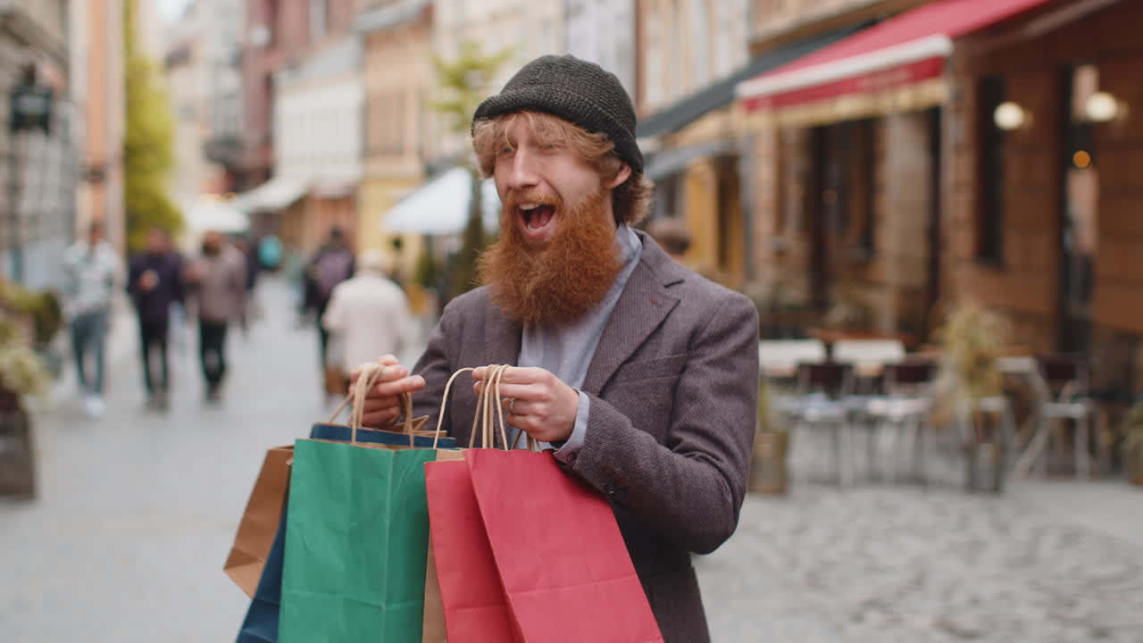 Happy young man shopaholic consumer after shopping sale with full bags walking in city street