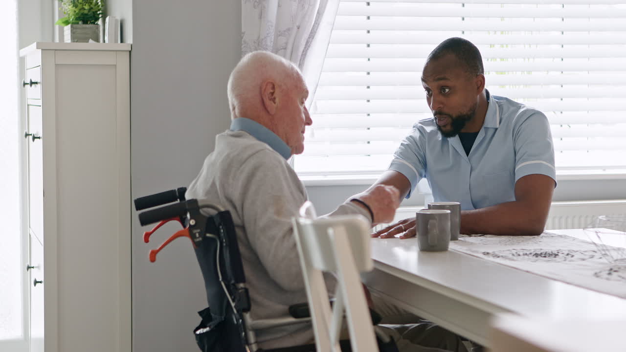 Elderly man in wheelchair talking with caregiver at home