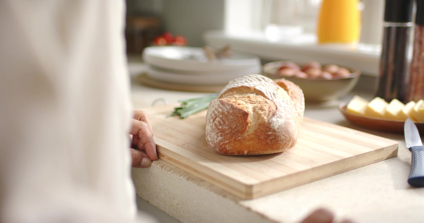 African American woman left hand gripping and steadying cutting board by window with bread to serve