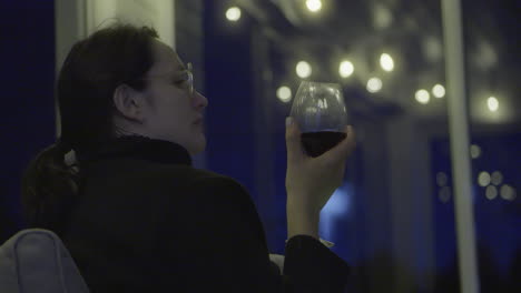 woman enjoys a glass of wine outdoors at night, surrounded by warm string lights