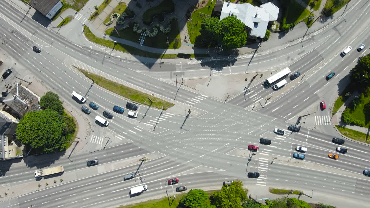 Top down aerial drone footage view of a busy intersection where cars, vehicles and buses are visible driving between white road markings. Pedestrians, people and cyclist are moving on zebra crossings.