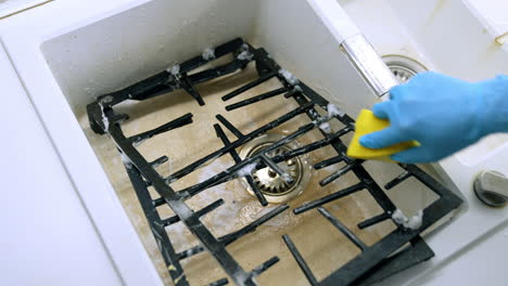 cleaning stove grates with soapy water. using a sponge and soapy water, a person cleans stove grates submerged in a kitchen sink filled with water