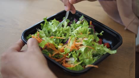 person eating salad in a black container