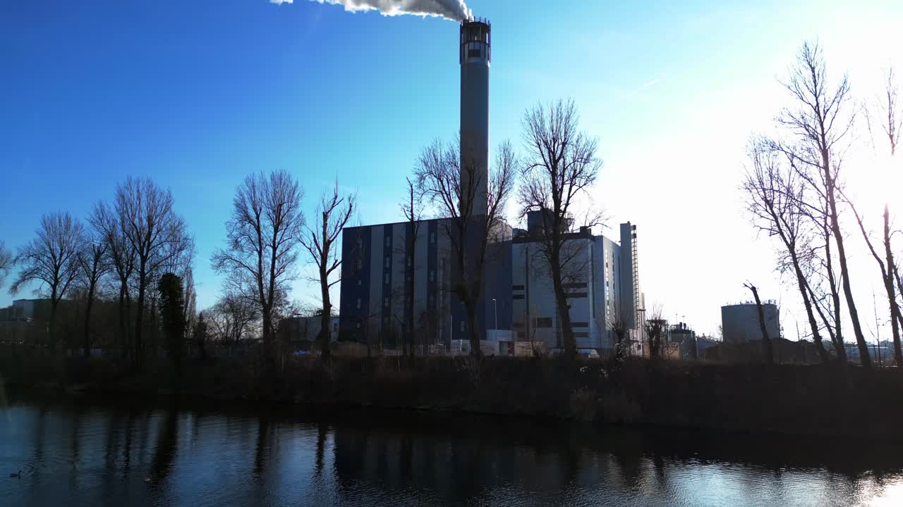 Waste to energy plant emitting smoke from its chimney, located near an urban area, environmental impact of waste. pull in drone