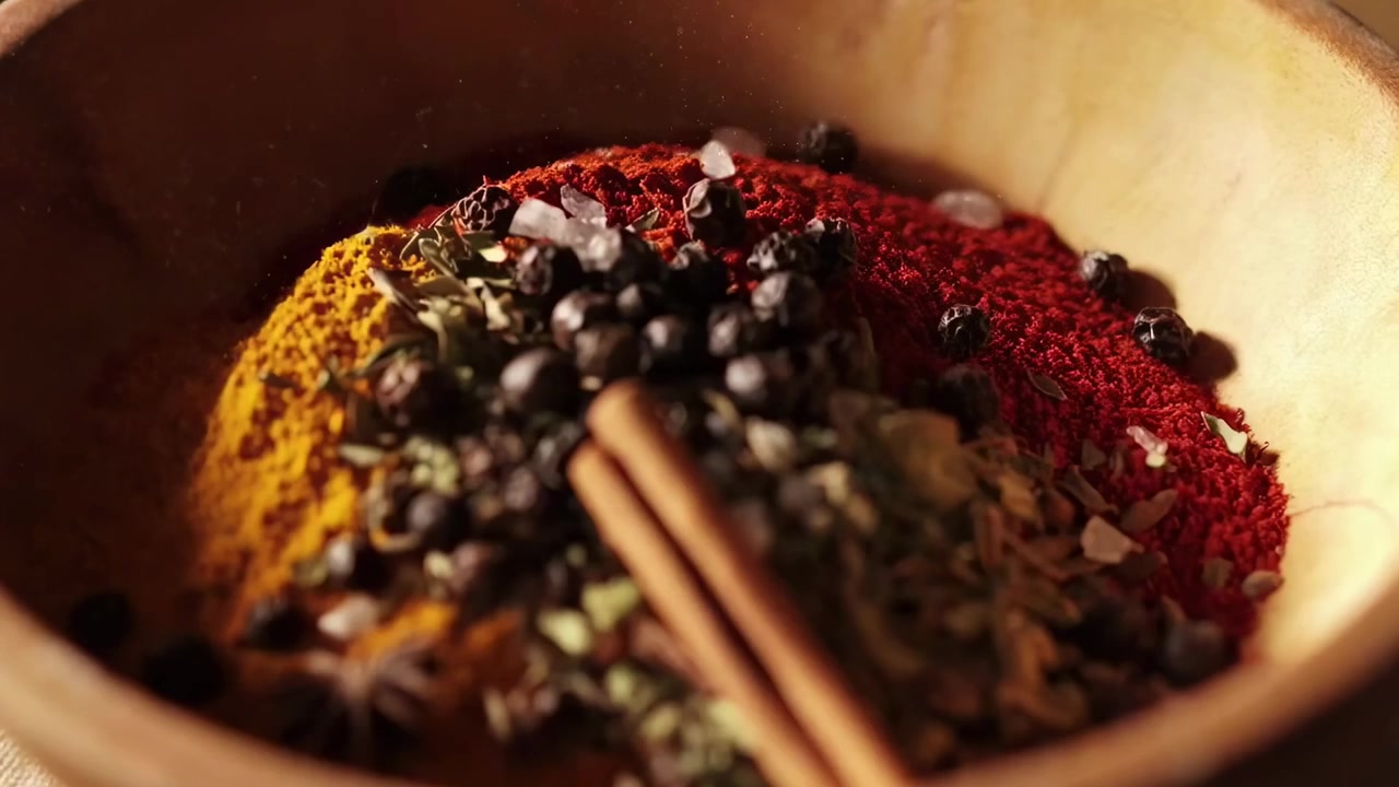 Primer plano de varias especias aromáticas siendo vertidas y mezcladas en un cuenco de madera