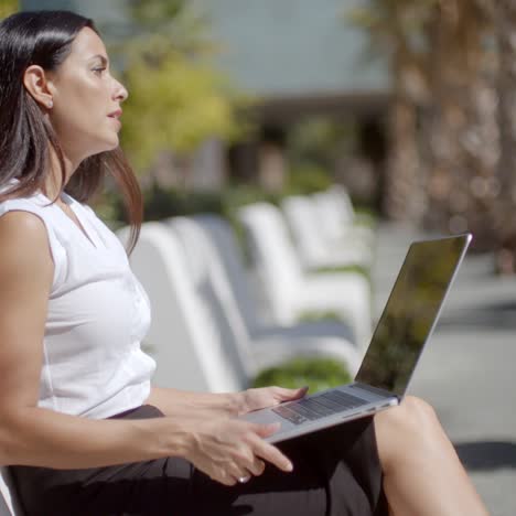 Atractiva-Mujer-Sentada-En-Un-Banco-Con-Una-Computadora-Portátil