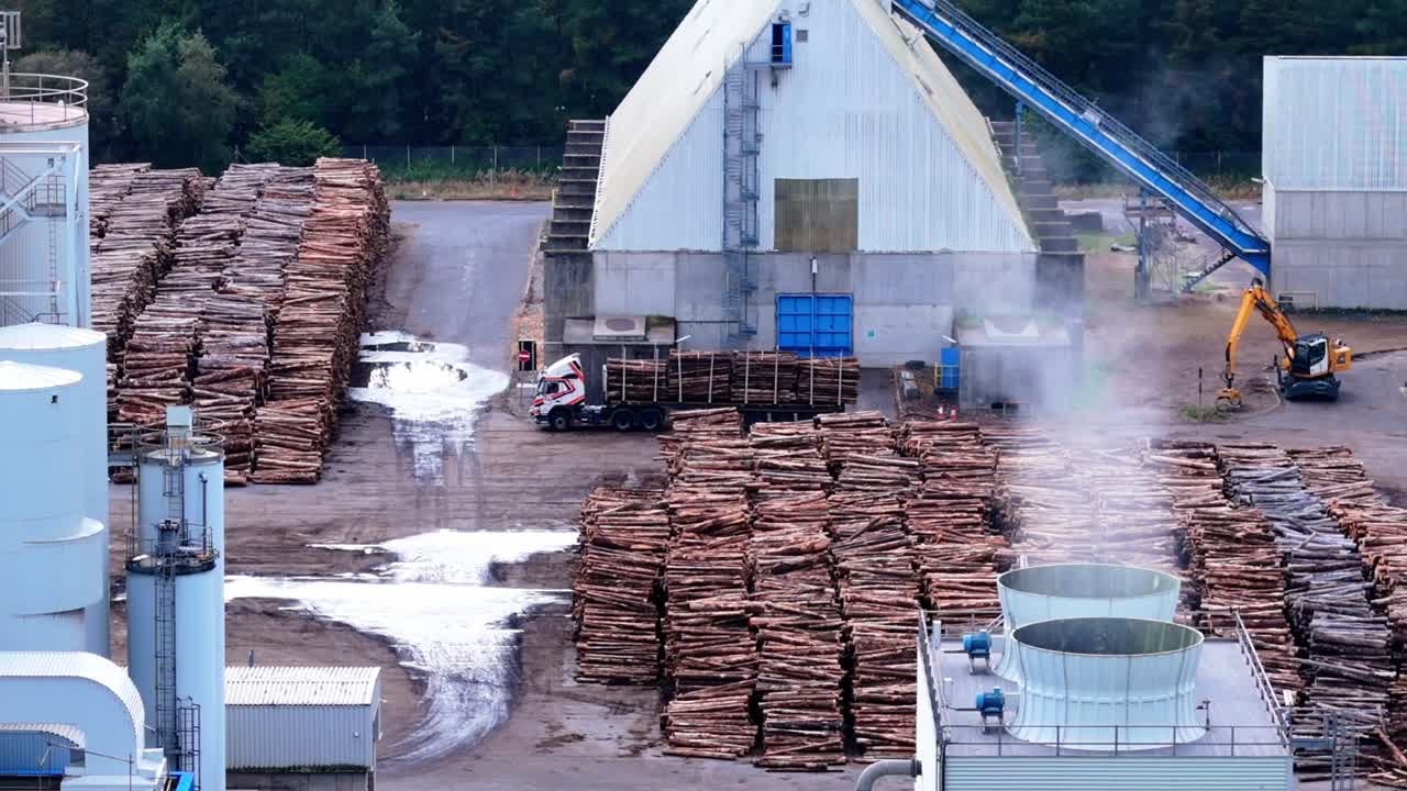 Aerial view of an industrial lumberyard with timber stacks, steam vents, and machinery loading logs. Captures forestry operations, timber supply chain, and heavy industry infrastructure