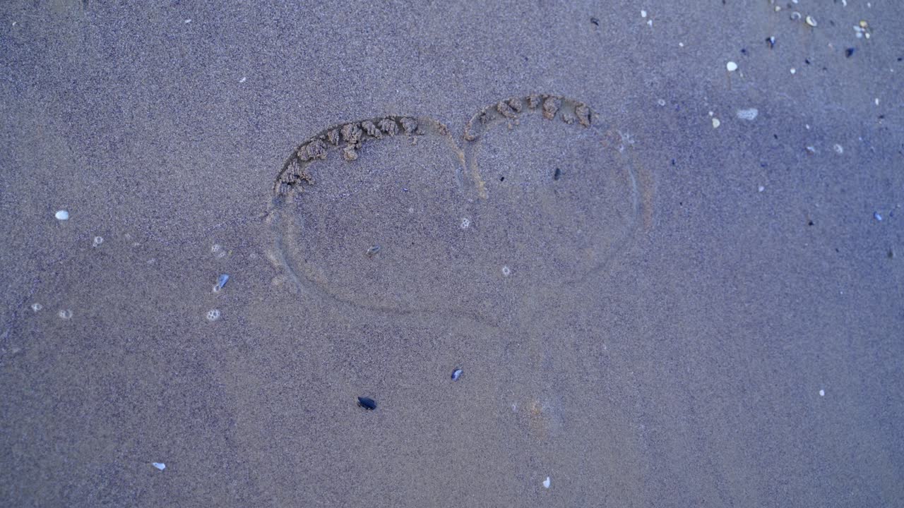 Girls hand draws a heart sign on a coastal sand, a holiday romance metaphor