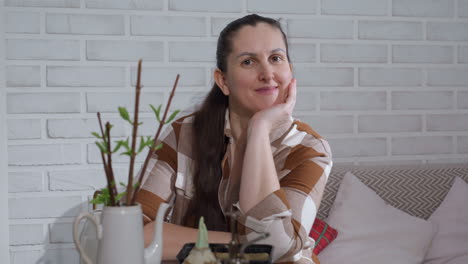 portrait view of botanical nurturer resting head on hand while leaning over glass table adorned with sprouting stems and gardening tools against brick wall backdrop offering serene plant care vibe