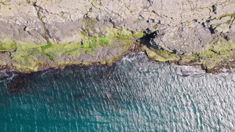 a rocky coastline with moss-covered stones and turquoise water in the faroe islands