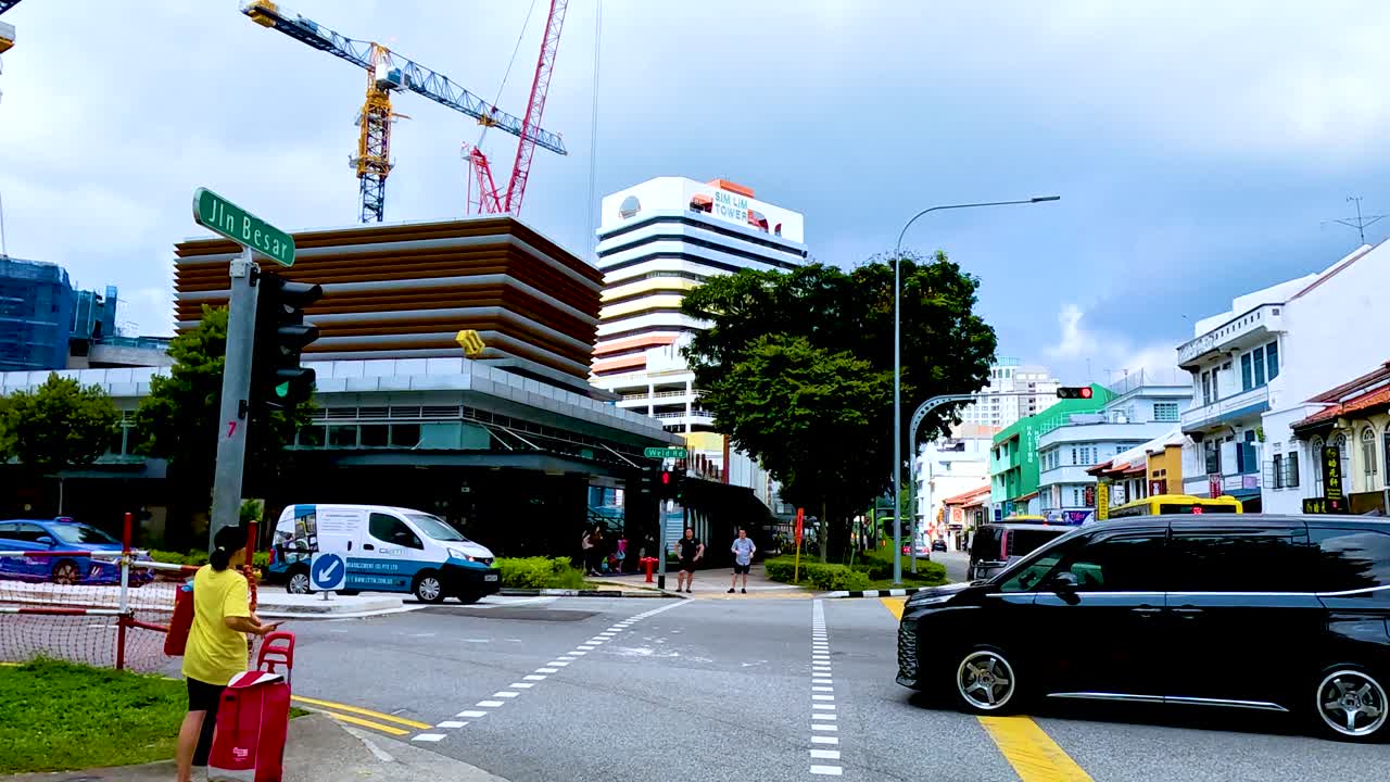 Person crosses street at city intersection with construction, traffic, and modern buildings in daylight