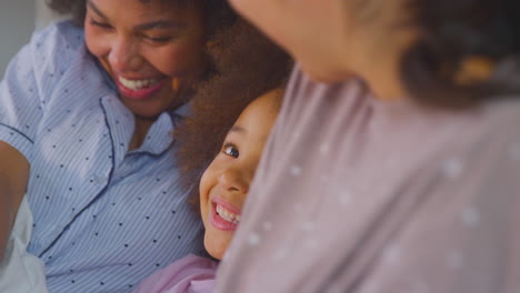 Family-With-Two-Mums-Wearing-Pyjamas-Playing-Lying-In-Bed-At-Home-With-Daughter