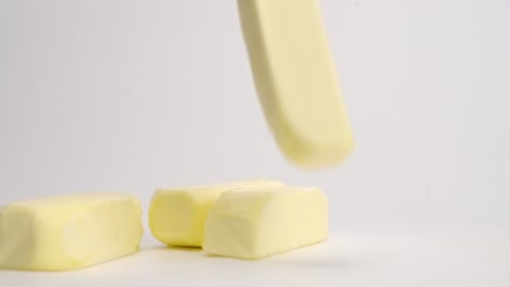 whole, unwrapped sticks of yellow butter cubes falling and bouncing onto white table top in slow motion and landing in pile