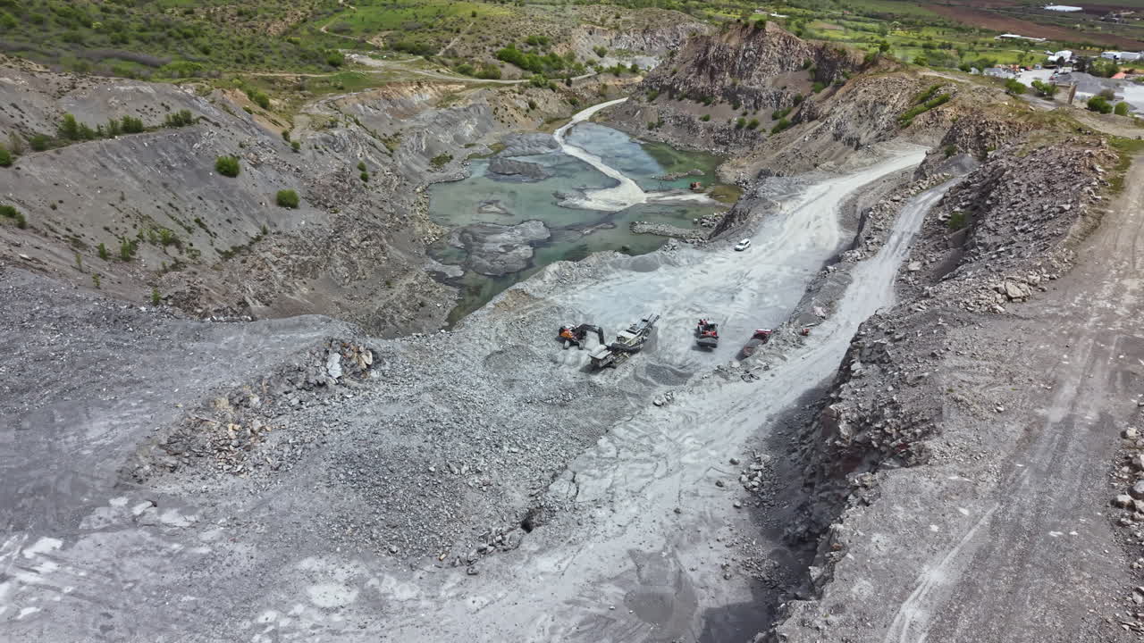 Construction workers use heavy machinery for mining operations in a large quarry located in a rural area during daylight hours