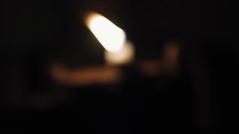 the woman holds a burning candle flame against blurred bokeh lights at dark background, close up