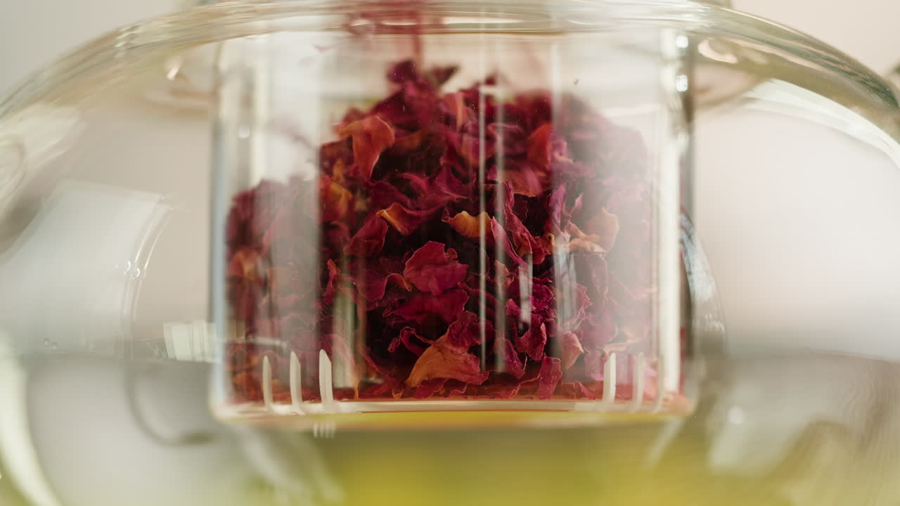 Dried Rose Petals Falling into a Glass Tea Infuser