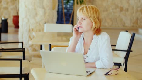 Business-Woman-On-Vacation-Sits-By-The-Laptop-Talking-On-The-Phone-In-Light-Summer-Clothes