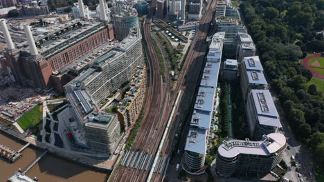 High-angle-view-of-train-driving-on-multi-track-railway-line-leading-between-apartment-houses-at-Battersea-Power-Station.-Tilt-up-reveal-cityscape.-London,-UK