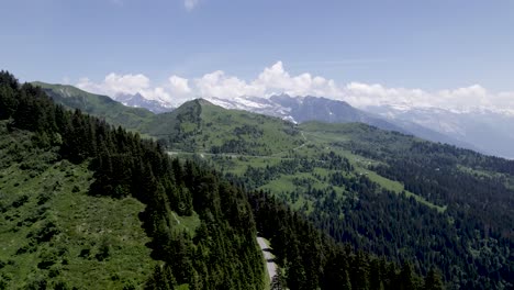 Movimiento-Aéreo-Hacia-Atrás-Con-Vista-A-La-Carretera-En-Las-Montañas-De-Los-Alpes-Franceses-Con-Montañas-Nevadas-Masivas-Y-Eternas-Del-Mont-Blanc-En-El-Fondo