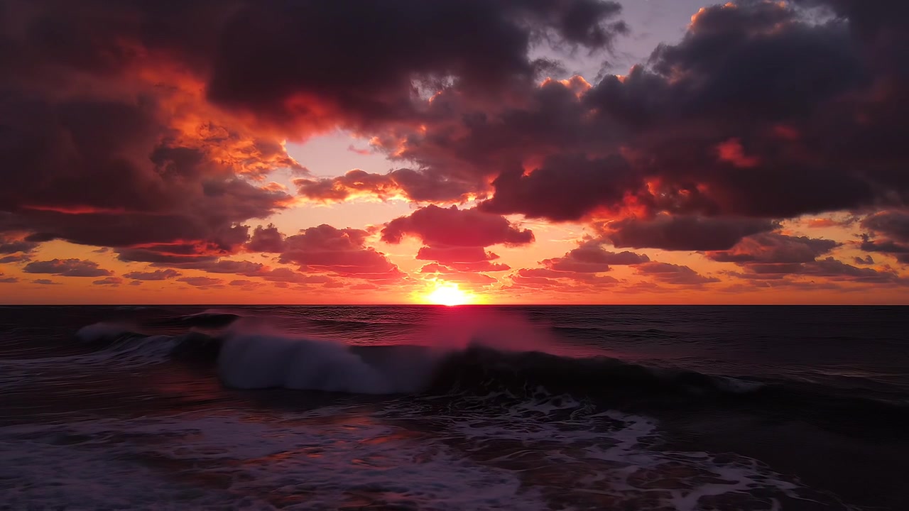 Dramatic sunset over ocean waves with vibrant red sky
