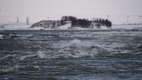 Wide-shot-of-flooding-river-during-snowy-winter-day-with-clouds-at-sky-in-Iceland