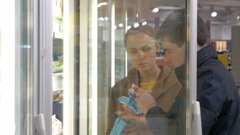 una pareja joven tomando productos en la sección de refrigeradores.