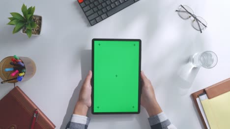 vista de arriba hacia abajo de una computadora portátil con pantalla verde simulada pantalla chromakey en un escritorio de oficina de madera al lado de la libreta con bolígrafos, gafas y un vaso de agua.