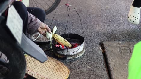 person roasting corn over a charcoal grill