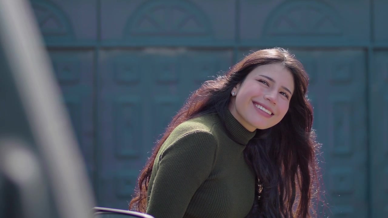 Portræt af en smilende brunette kvinde med langt hår, der blæser i vinden, udendørs i naturligt lys.