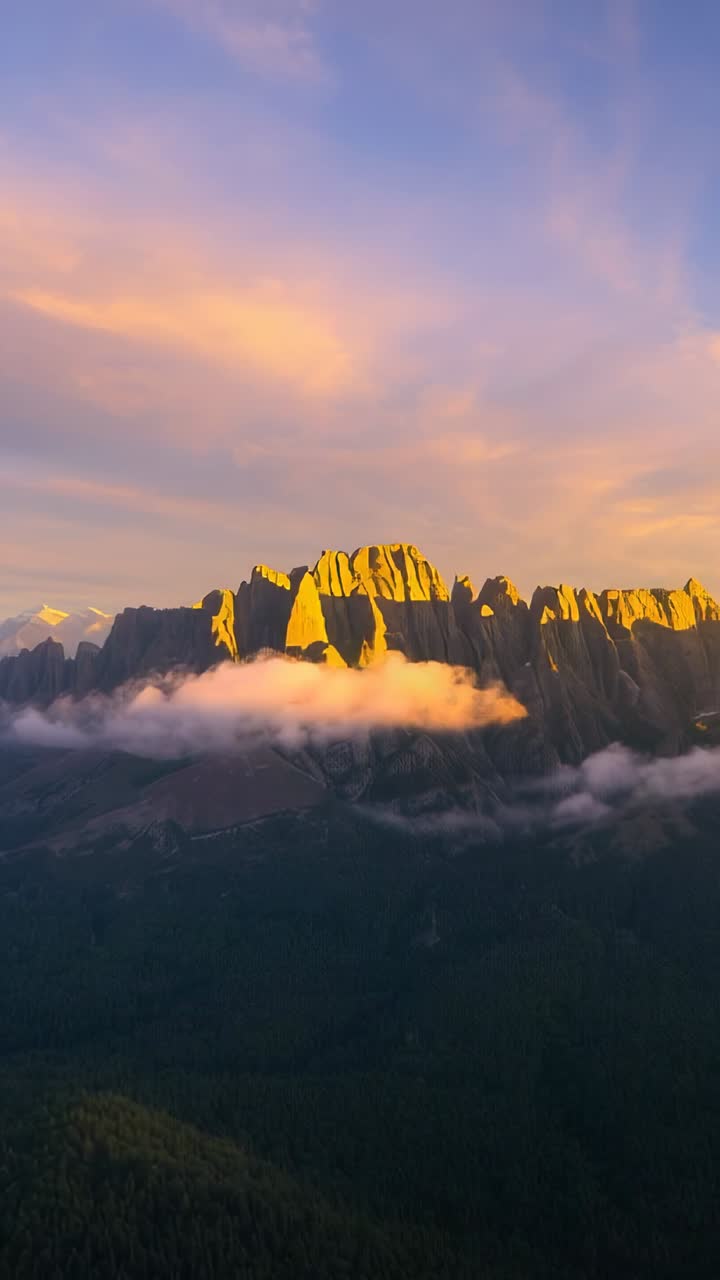 Vertical video: Pouring sunrise light on mountain ridge in forested valley with drifting clouds