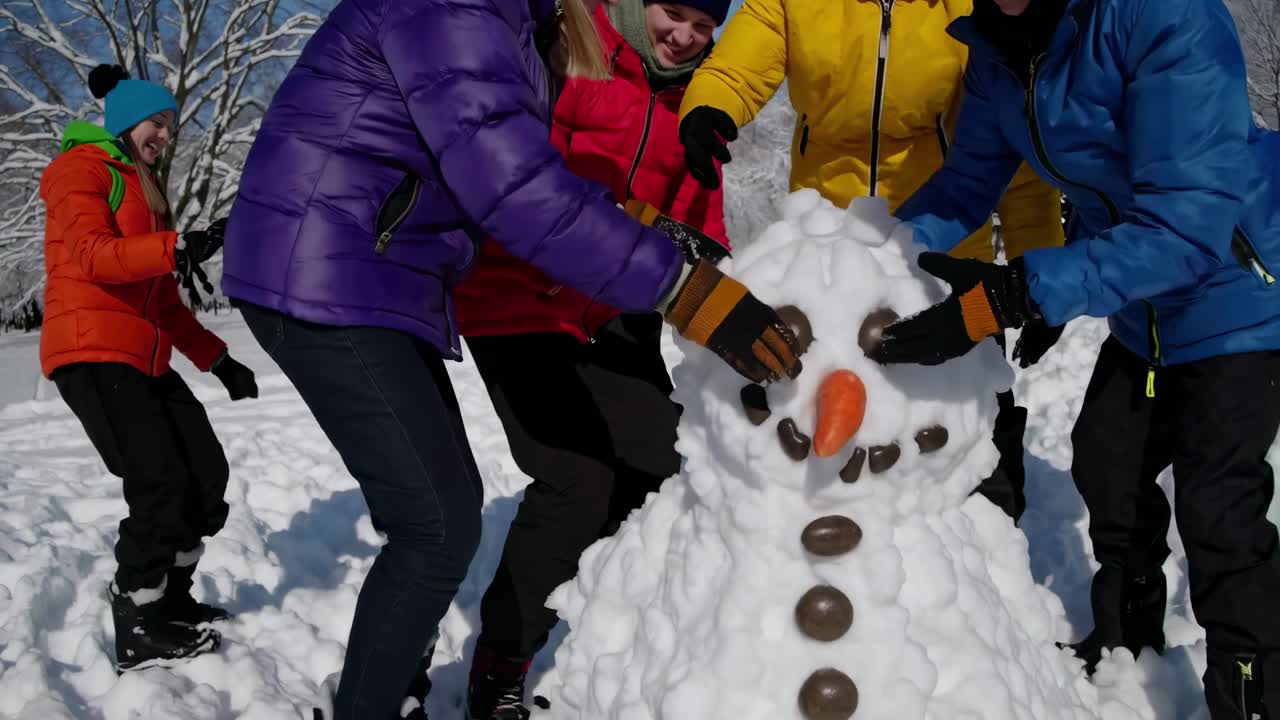 A lively video captures friends building a snowman, shot from a low angle, highlighting colorful
