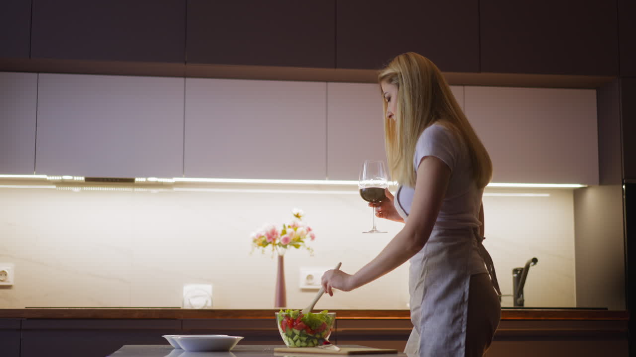 Donna mescola insalata e beve vino rosso preparando la cena a casa