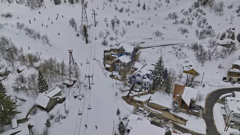 Park-City-Utah-Vista-Aérea-V73-Vista-Aérea-Sobrevuelo-De-Casas-En-La-Ladera-Hacia-El-Centro-De-La-Ciudad-Capturando-A-Personas-Esquiando-En-Las-Laderas-Nevadas-Rodeadas-De-árboles-Cargados-De-Nieve---Filmado-Con-Cine-Mavic-3---Febrero-De-2023