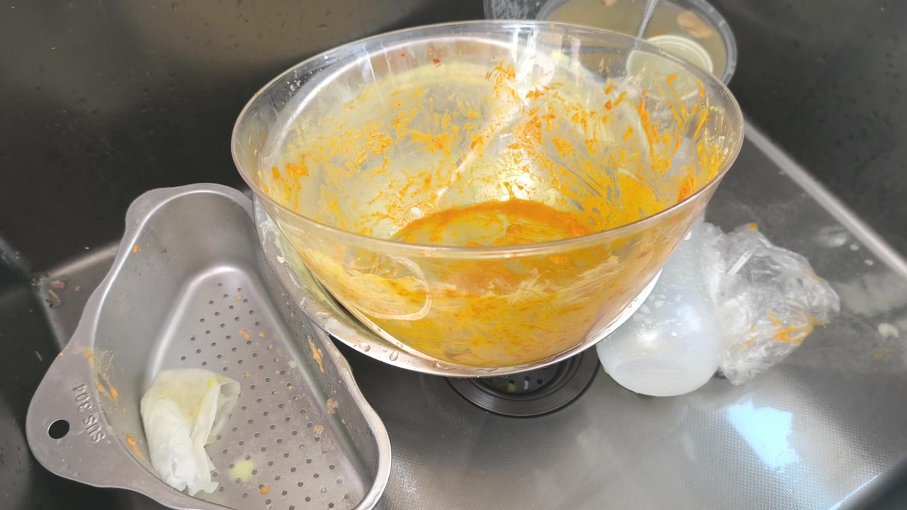 Dirty dishes and bowls are piled inside a kitchen sink. Leftover food scraps remain unwashed on the surface. Cleaning them is essential to maintain hygiene and a tidy home.