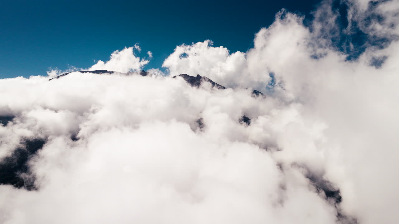 Drone flying over white clouds covering Mount Agung top with blue sky in background, active volcano in Bali, Indonesia