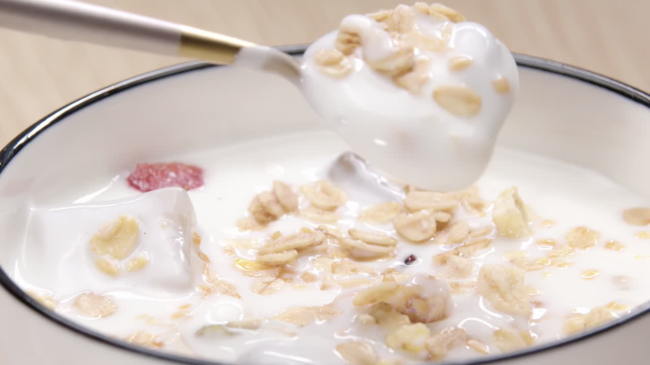Cucchiaio di metallo che raccoglie delicatamente yogurt bianco cremoso e denso ai cereali da una ciotola rustica, dalla consistenza e dall'aspetto delizioso e salutare, perfetto per la colazione o uno spuntino, che enfatizza la freschezza del latticino.