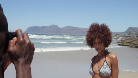 vista lateral de un joven afroamericano tomando fotos de una mujer con una cámara digital en la playa 4k