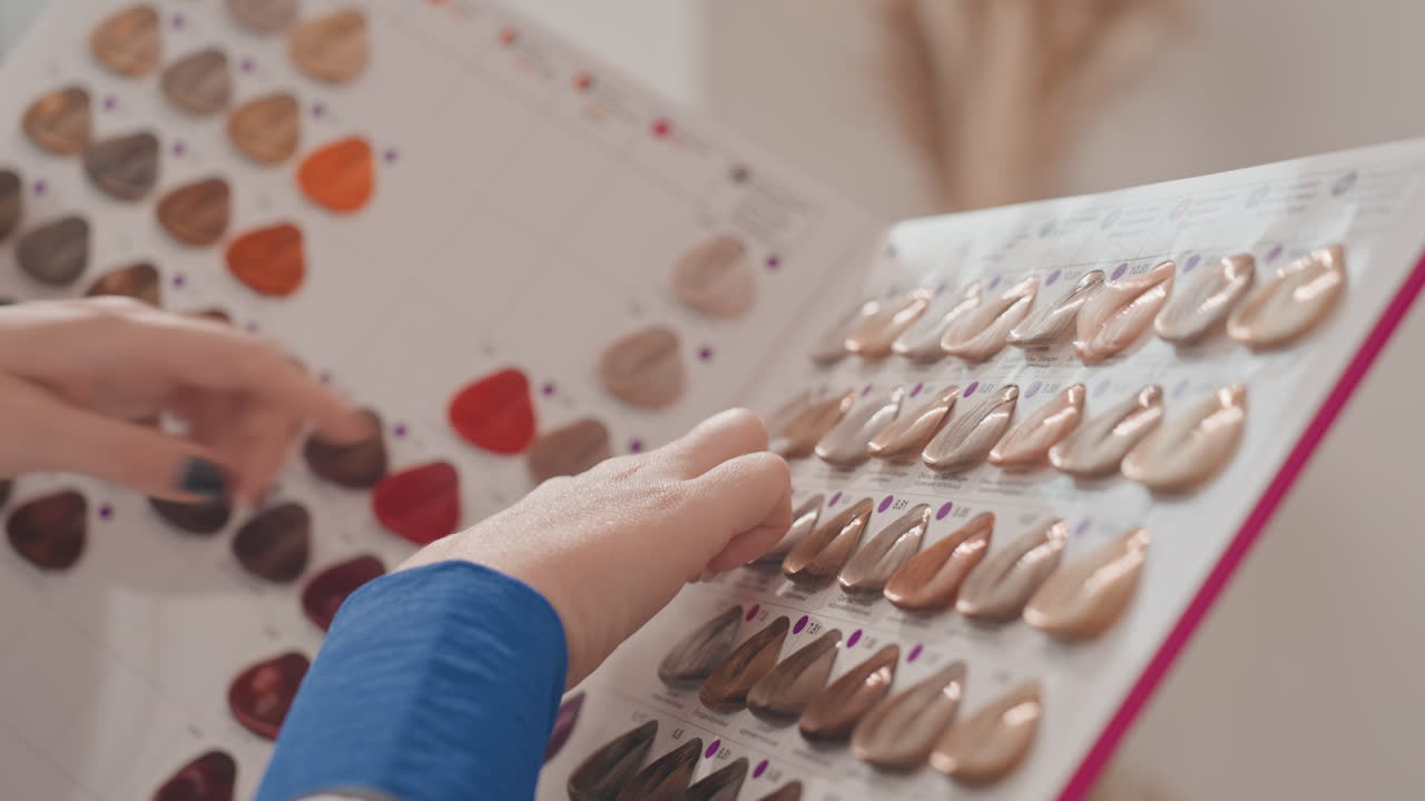 Hands selecting nail polish swatches on board. Closeup of tattooed client hand and manicurist examining neutral and nude shades, glossy and matte finishes, organized palette on display, warm natural