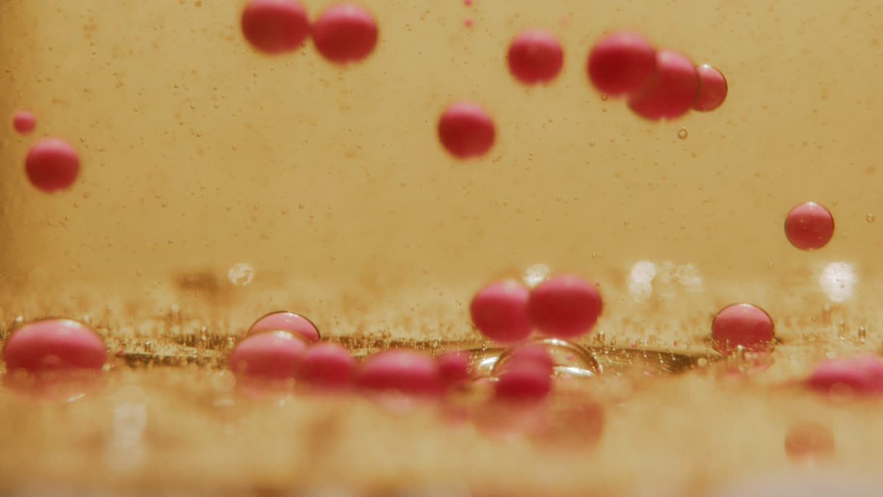 Pink Ink bubbles sinking down in oil gathering at the bottom of the frame