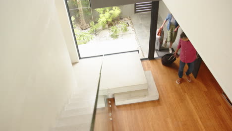 entering home, woman carrying luggage while man holding door open, copy space