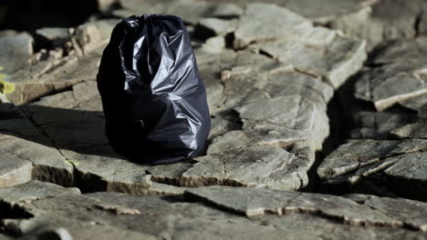 black trash bag lay on a rocky beach