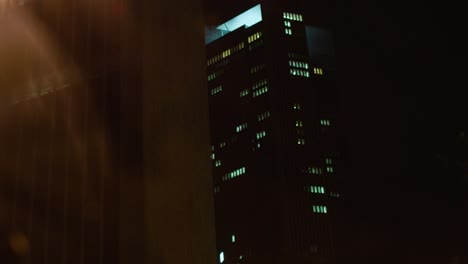 Nighttime-view-of-an-illuminated-office-building-from-a-moving-car,-capturing-the-essence-of-urban-life-after-dark