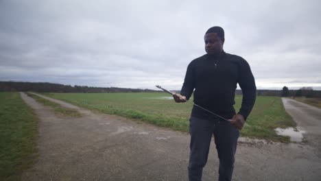 Modern-Black-Swordsman-Warrior-Awaiting-Battle-Opponent-in-Open-Field-Under-Grey-Sky,-Europe,-4K-|-Muscular,-Intimidating,-Shadow,-Figure,-Blurry,-Dark-Clothes,-Powerful,-Sword,-Examine,-Found,-Hands