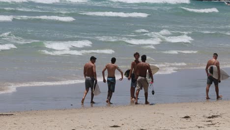 group of surfers walking with surfboards on sandy beach