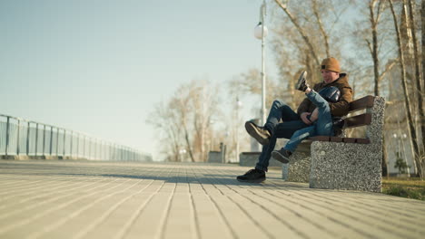 a father and son sit closely on a park bench as he holds him closely, the father stretches his right leg and the son his left leg playfully, as the boy adjust himself on the bench