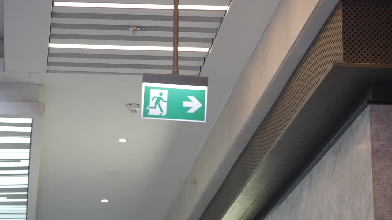 Señal verde de salida de emergencia colgada de un techo moderno